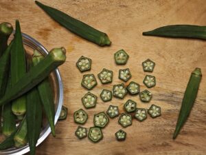 Top view of fresh and sliced okra (Abelmoschus esculentus) on a wooden surface, showcasing natural textures and colors.