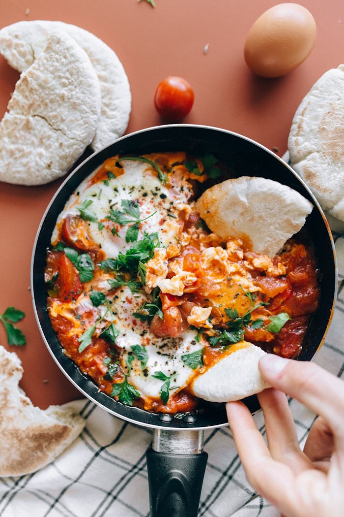 About Savor a classic Shakshuka dish with vibrant tomatoes, eggs, and herbs served with fresh pita bread.